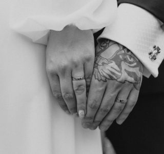 Close-up shot of married couple holding hands with rings, showcasing tattoos.